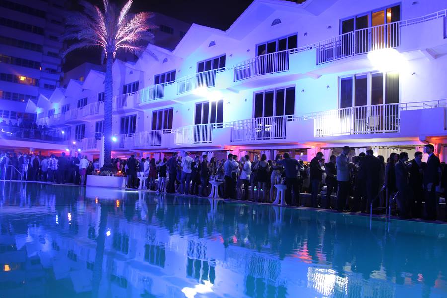 Guests lining the Delano pool at night with the hotel facade lit deep blue