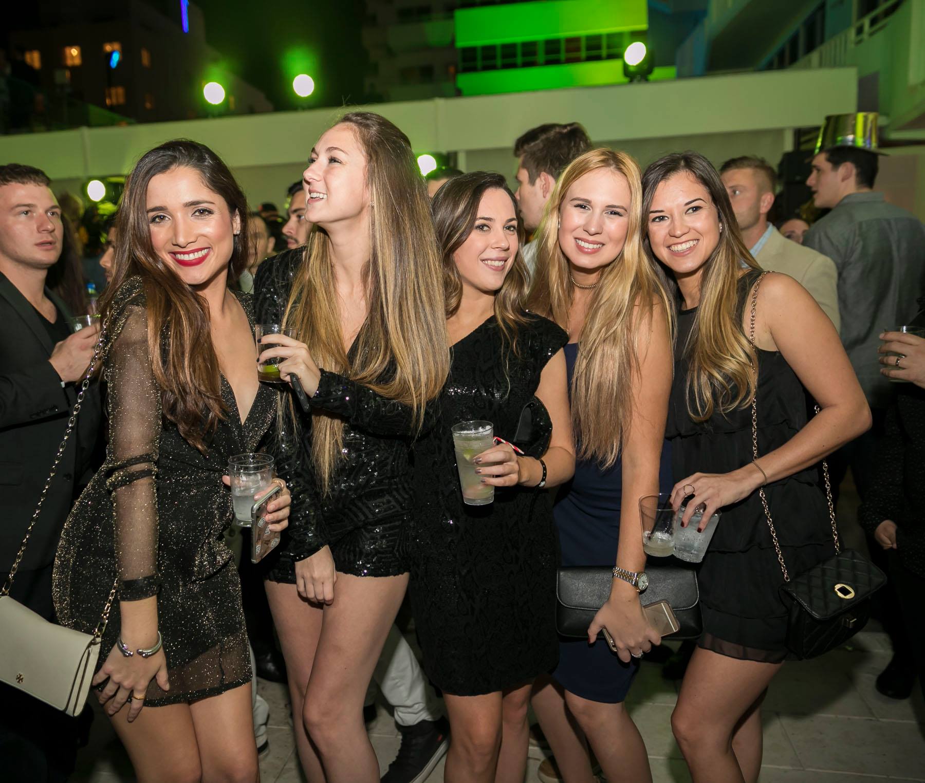 Five guests in black dresses posing together on the green-lit rooftop
