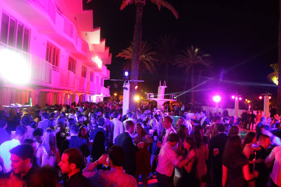 Packed Delano pool deck at night with the hotel facade washed in hot pink