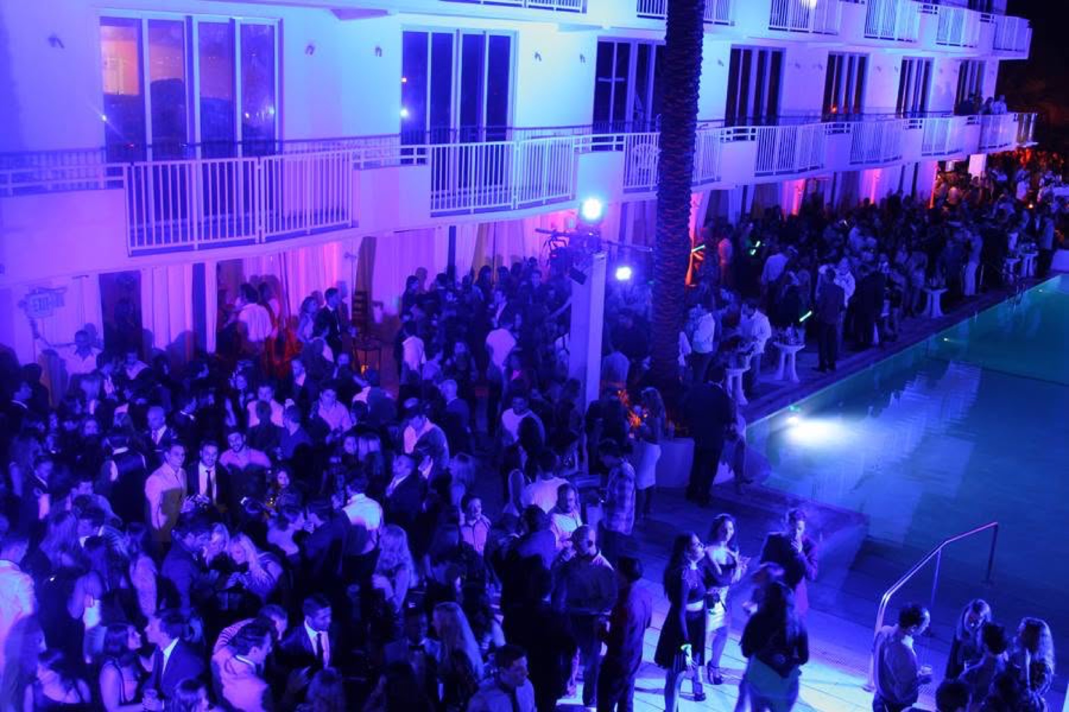 Aerial view of the pool-deck crowd beneath the blue-lit facade