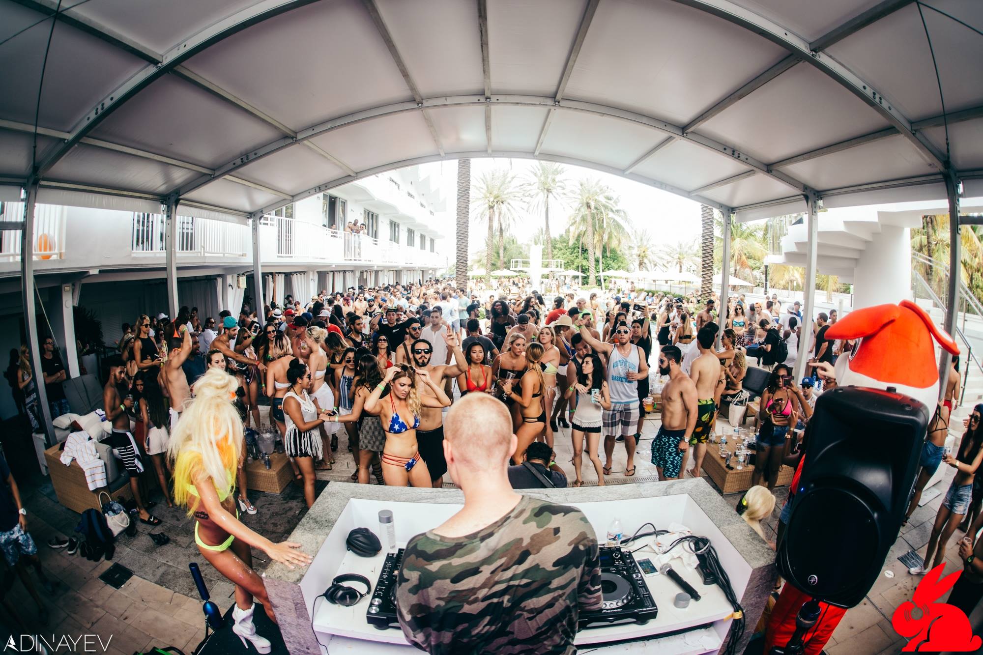 Fisheye view from behind the DJ booth over a packed daytime pool crowd with the Red Rabbit mascot