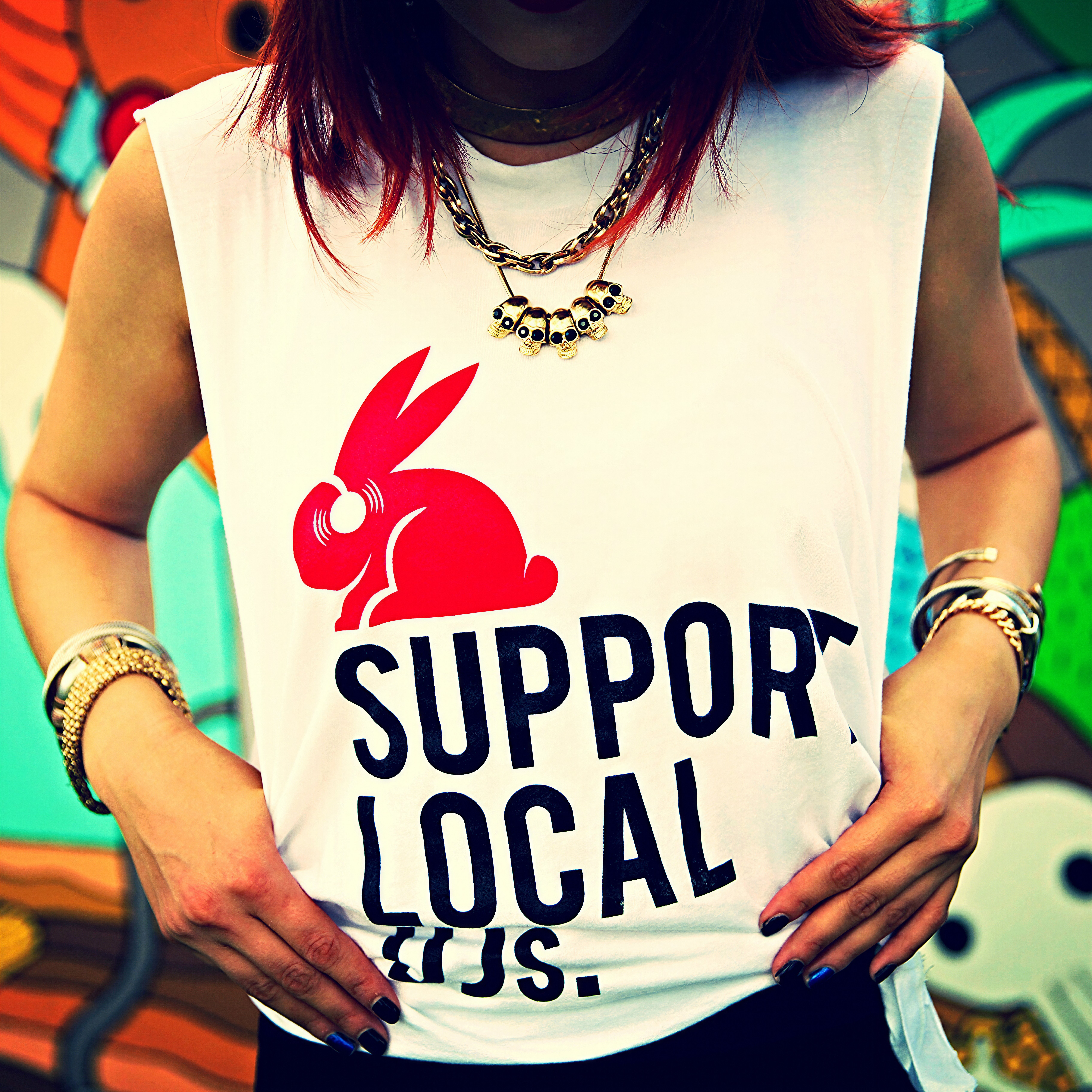Guest in a white Red Rabbit Support Local tee standing in front of a colorful street mural