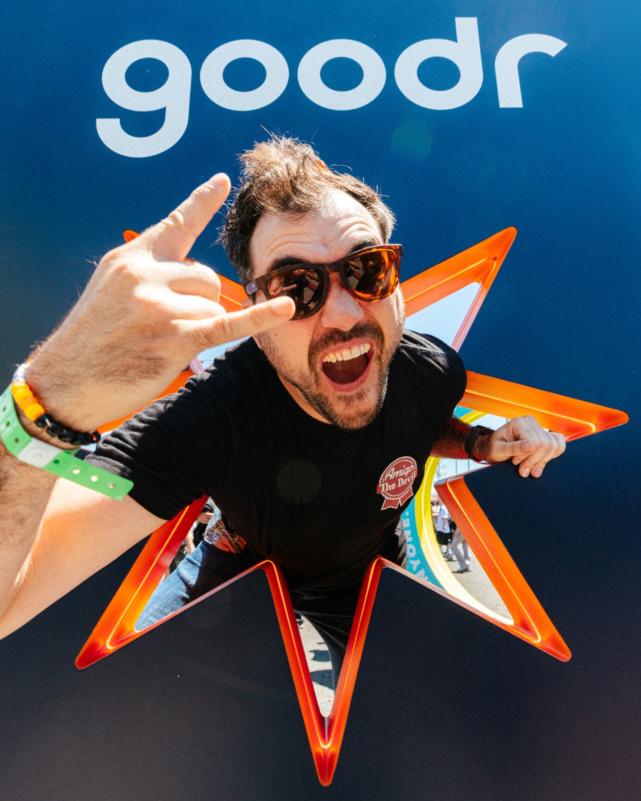 Festivalgoer throwing the horns through a glowing goodr star prop against a deep blue wall